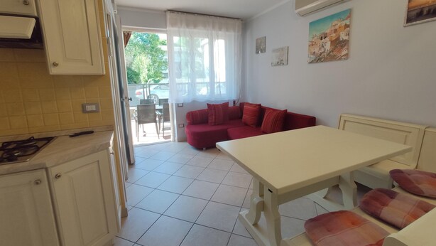 Una cocina con armarios blancos, una mesa de comedor con sillas, un sofá rojo y un cuadro en la pared.