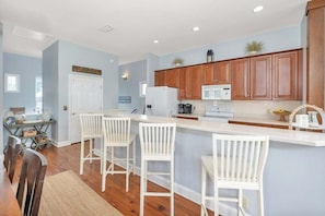 A modern kitchen with wooden cabinets, a white island with bar stools, and a dining area with a wooden table and chairs.