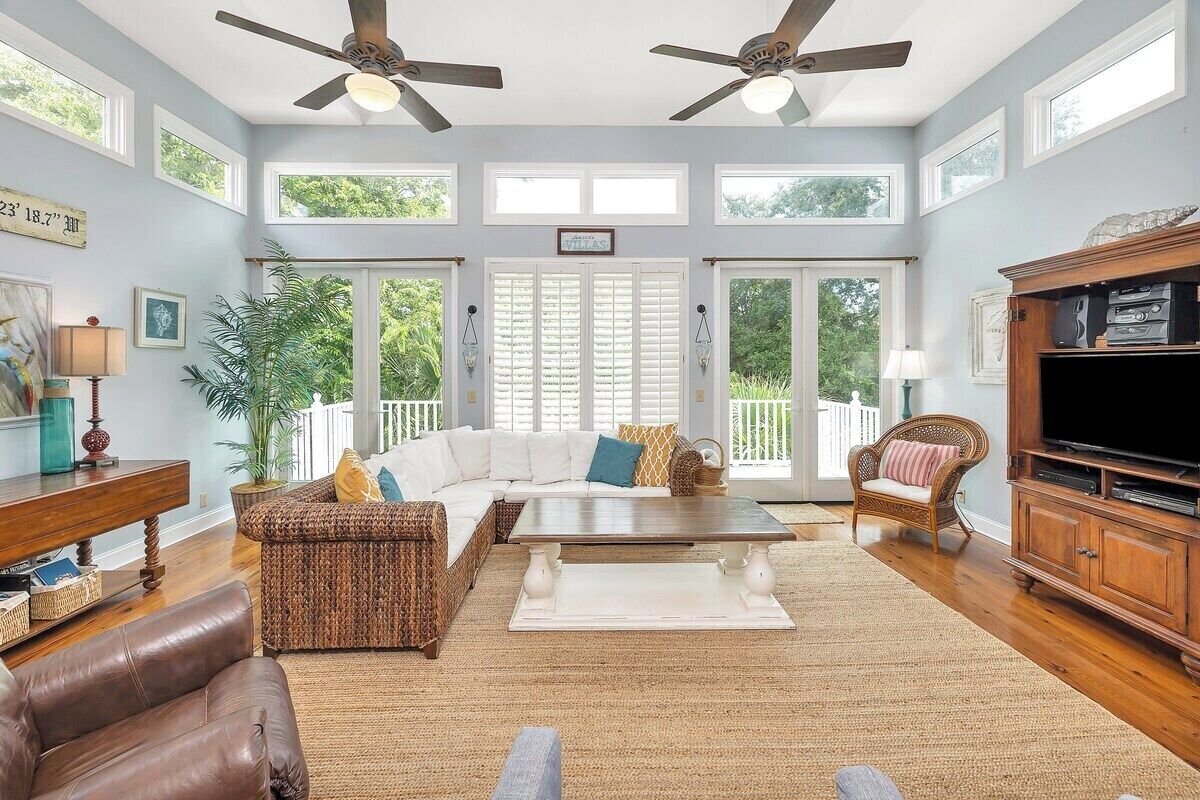 A spacious living room with a white sofa, a brown wicker chair, a wooden coffee table, and a television on a wooden stand.