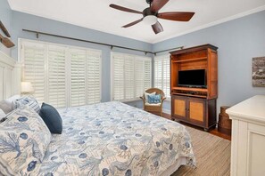 A bedroom with a bed, a ceiling fan, a TV on a wooden cabinet, and a chair.