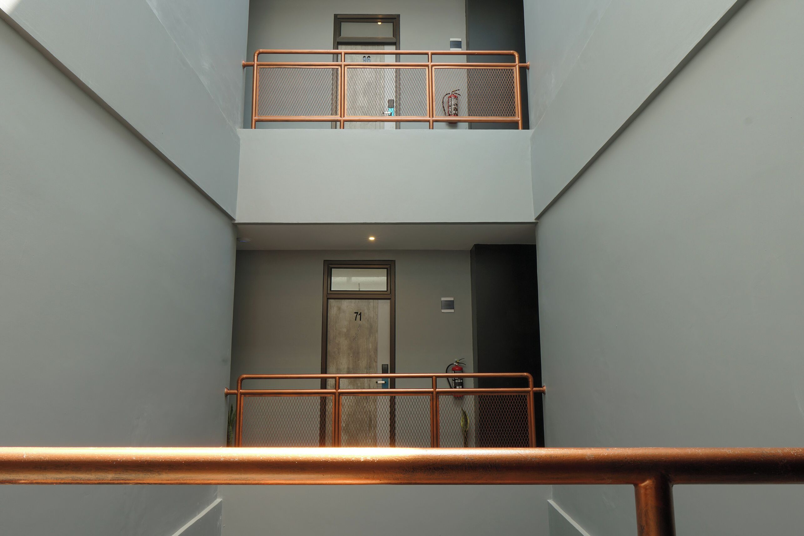 Een meerlaags interieur met een metalen leuning, een deur met de aanduiding '71', en een brandblusser op de begane grond.