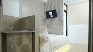 A modern bedroom with a brick wall, a mounted TV, a built-in bed, and a minimalist design. - Dparagon Menteng (Jakarta)