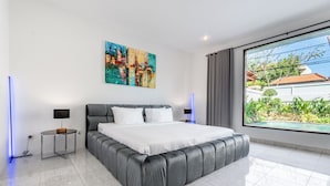 A modern bedroom with a large bed, a painting on the wall, and a view of a garden through the window. - Villa Sky View - Seminyak (Seminyak)