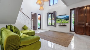 A spacious living room with a green sofa, a large flat-screen TV, and a view of mountains through the windows. - Villa Sky View - Seminyak (Seminyak)