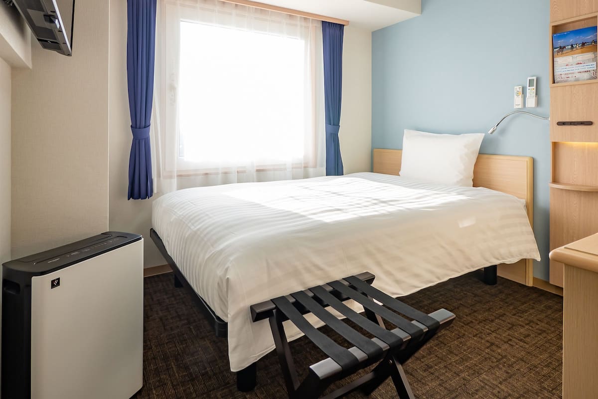 A hotel room with a bed, a desk, a chair, a TV, and a small fridge.
