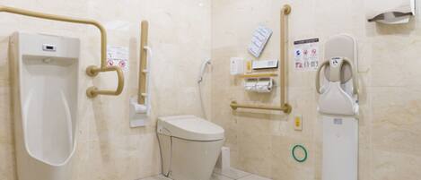 A men's restroom with a urinal, toilet, handrails, and a soap dispenser.