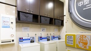 Une buanderie équipée de trois machines à laver, d’un sèche-linge et d’une balance fixée au mur.
