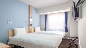 Une chambre d’hôtel avec deux lits, une table de chevet en bois, un bureau, un miroir, une fenêtre avec des rideaux et un téléviseur à écran plat fixé au mur.