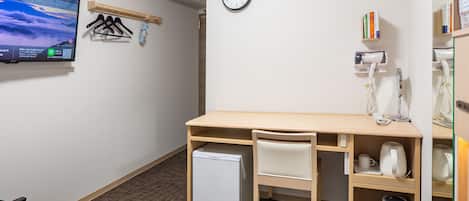 A hotel room with a bed, a desk with a chair, a small refrigerator, a clock, a TV, and a wall-mounted heater.