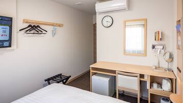 Habitación de hotel con cama, escritorio con espejo, refrigerador pequeño, calefacción, reloj y televisor montado en la pared.