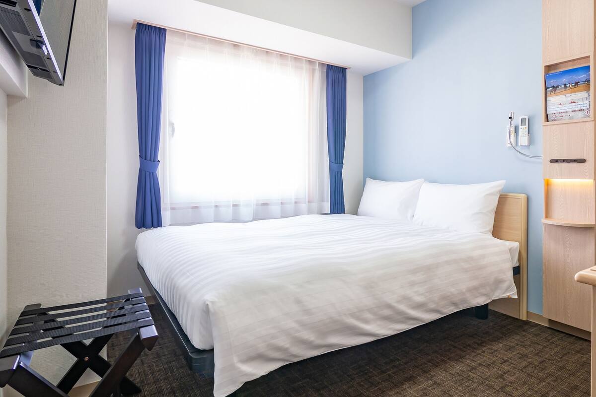 A hotel room with a bed, a desk, and a window with curtains.
