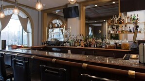 Eine Bar mit einer langen Theke, Barhocker und einer Auswahl an Flaschen und Gläsern auf Regalen.