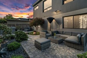 A modern outdoor patio with wicker furniture, a stone floor, and a view of a sunset.