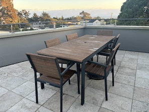 Eine Dachterrasse mit Holztisch und -stühlen, Blick auf die Stadt und einer Brüstung.