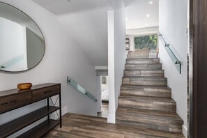 A modern staircase with wooden steps and glass railings, leading to a bedroom with a large window.