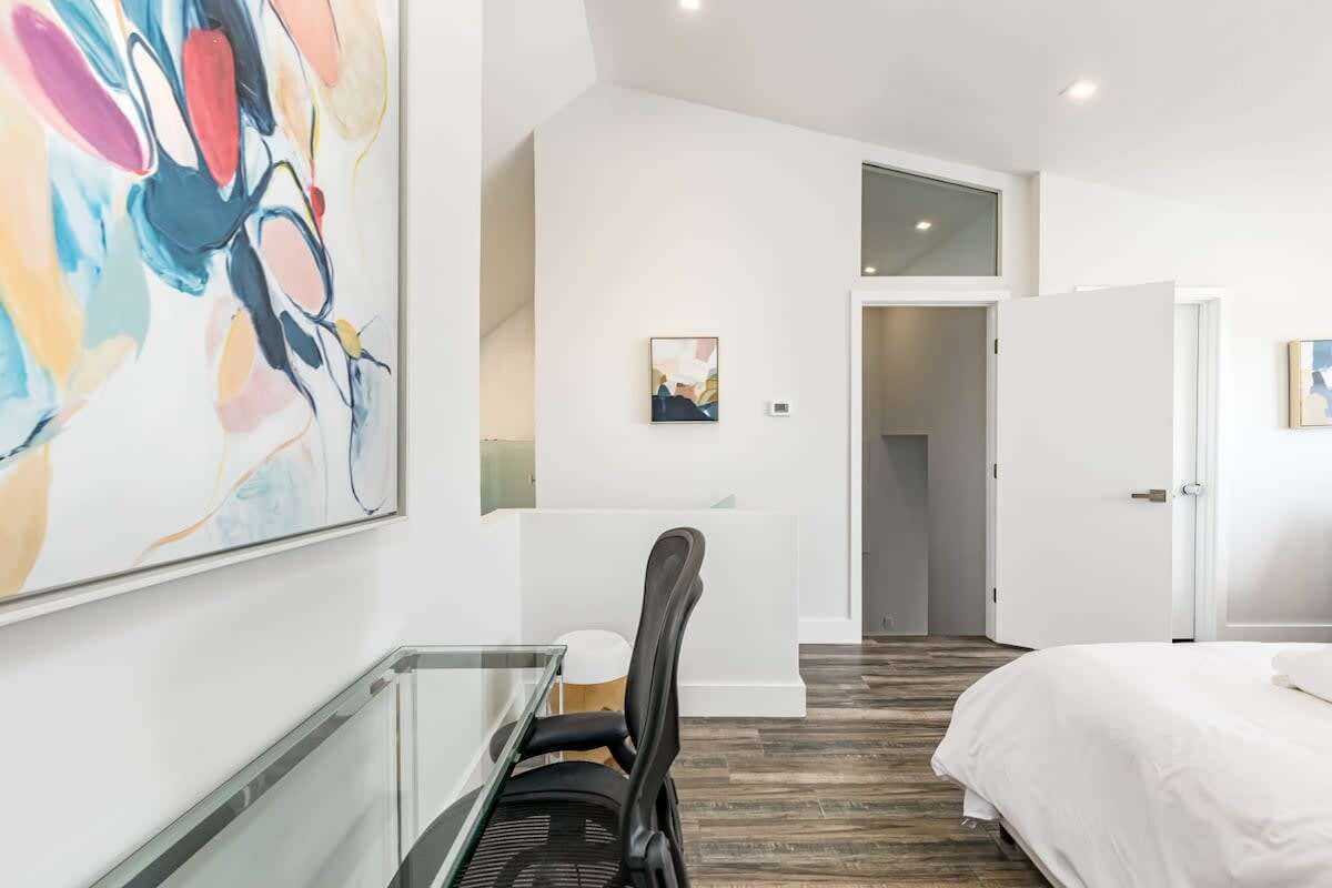 A hotel room with a bed, a desk with a chair, a large abstract painting, and a door leading to another room.