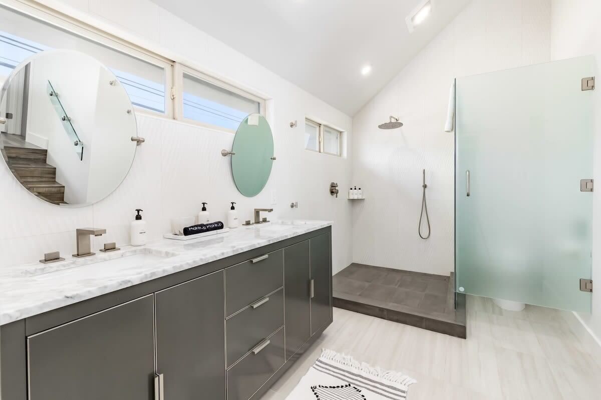 Une salle de bain moderne dotée d’un grand miroir, d’une douche et d’un meuble-lavabo avec un plan de travail en marbre.