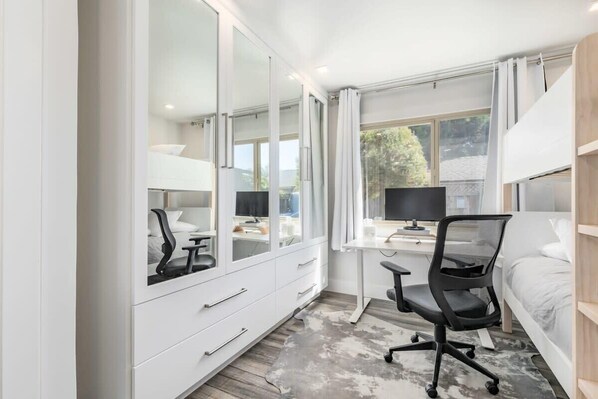 A modern bedroom with a large mirror, a desk with a computer, a chair, and a bed.