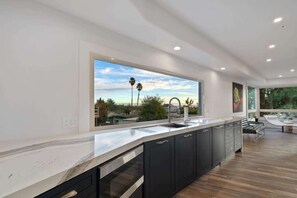 A modern kitchen with a large window, dark cabinetry, and a marble countertop.