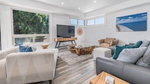 A modern living room with a large TV, comfortable seating, and a view of the outdoors. - Luxury Aptos Home - Ocean Views & Hot Tub! (Aptos)