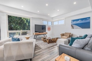 A modern living room with a large TV, comfortable seating, and a view of the outdoors.