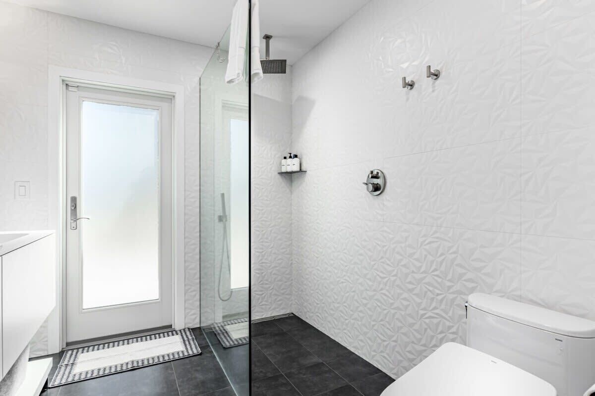 Une salle de bain moderne avec une douche à parois de verre, des toilettes blanches et un mur à motifs.