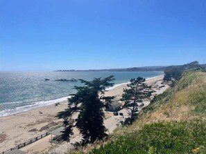 A coastal view with a beach, a parking area, and a grassy hill.