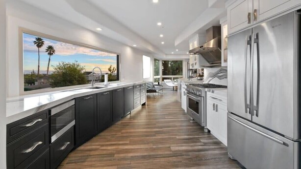 A modern kitchen with dark cabinets, stainless steel appliances, and a large window overlooking a scenic view. - Luxury Aptos Home - Ocean Views & Hot Tub! (Aptos)