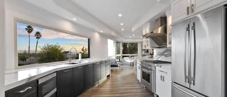 A modern kitchen with dark cabinets, stainless steel appliances, and a large window overlooking a scenic view.