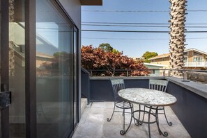 A balcony with a table and chairs, a palm tree, and a view of buildings and trees.
