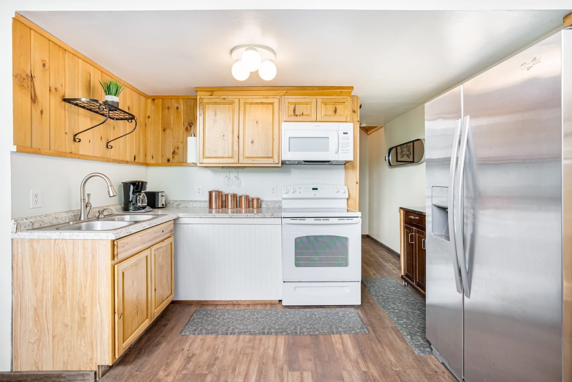 A kitchen with wooden cabinets, a white stove, a microwave, a sink, and a stainless steel refrigerator.