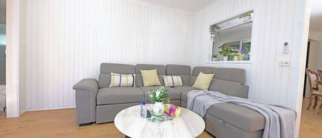 A modern living room with a grey sectional sofa, a round coffee table, and a window with plants.