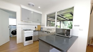 A modern kitchen with white cabinets, a built-in oven, a microwave, and a large window. - Melbourne 4BRM Staycation Parkside (Hallam)
