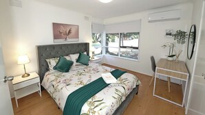 A bedroom with a bed, bedside table, lamp, and a desk with a chair. - Melbourne 4BRM Staycation Parkside (Hallam)