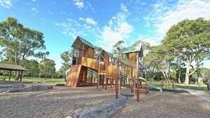 A playground with wooden climbing structures and a slide. - Melbourne 4BRM Staycation Parkside (Hallam)