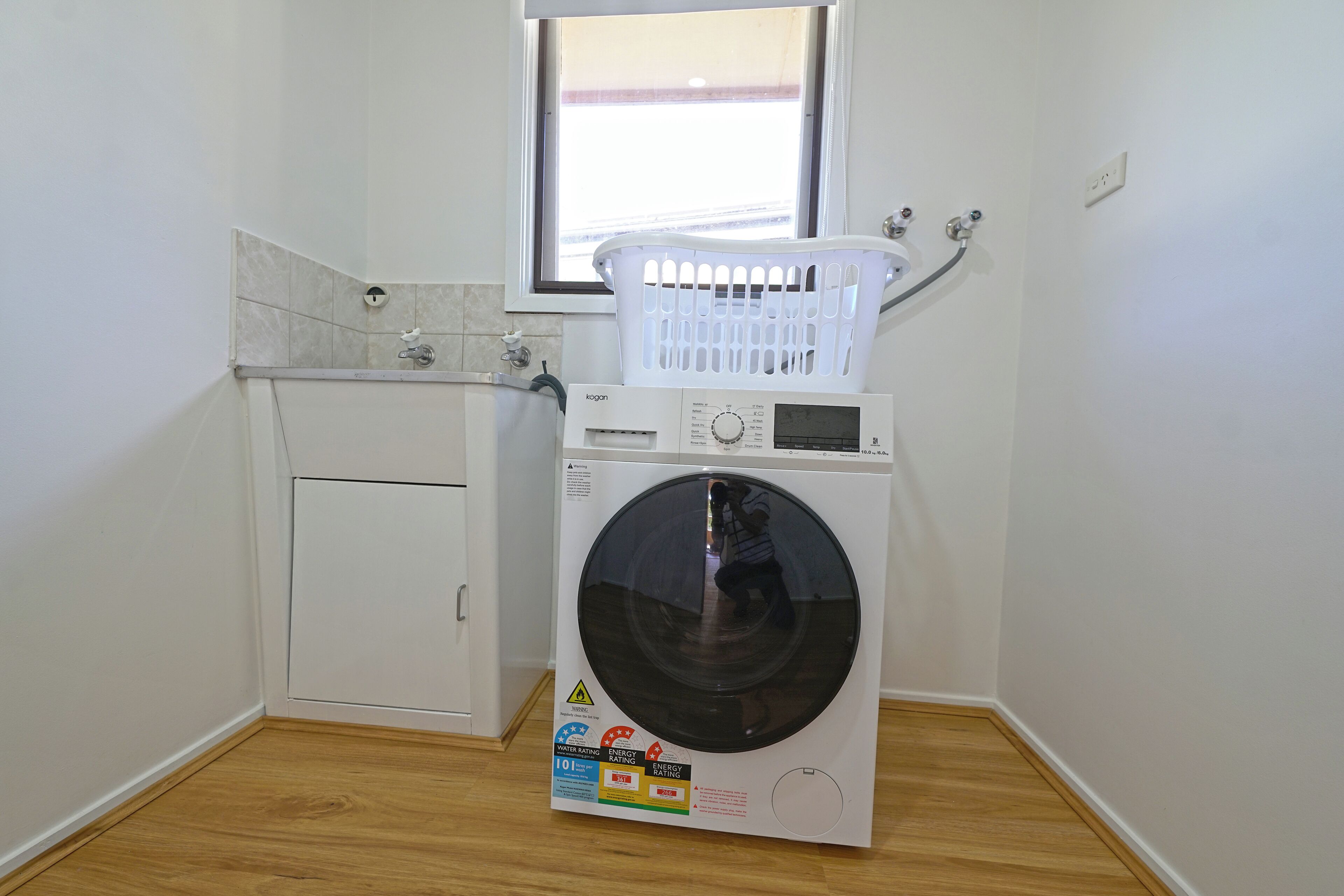 A compact laundry room with a front-loading washing machine, a white laundry basket on top, and a small cabinet.