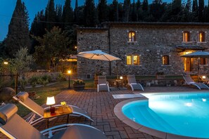 Un bâtiment en pierre doté d’une piscine, d’un espace extérieur aménagé pour s’asseoir et d’une terrasse bien éclairée.