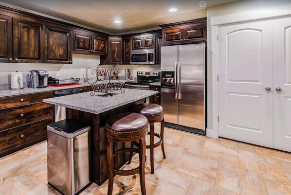 Una cocina con armarios de madera oscura, electrodomésticos de acero inoxidable, encimera de granito y una zona con taburetes de bar.