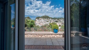 A view from a balcony with a stone wall and metal railing, overlooking a hillside with buildings and greenery. - Villa Albachiara in Capri (Capri)