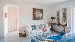 A living room with a white sofa, blue armchairs, a coffee table, a clock, and decorative wall art. - Villa Albachiara in Capri (Capri)