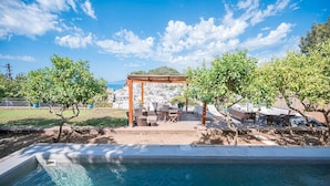 A pool area with a pergola, seating, and a view of a coastal town. - Villa Albachiara in Capri (Capri)