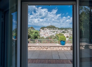A view from a balcony with a stone wall and metal railing, overlooking a hillside with buildings and greenery. - Villa Albachiara in Capri (Capri)