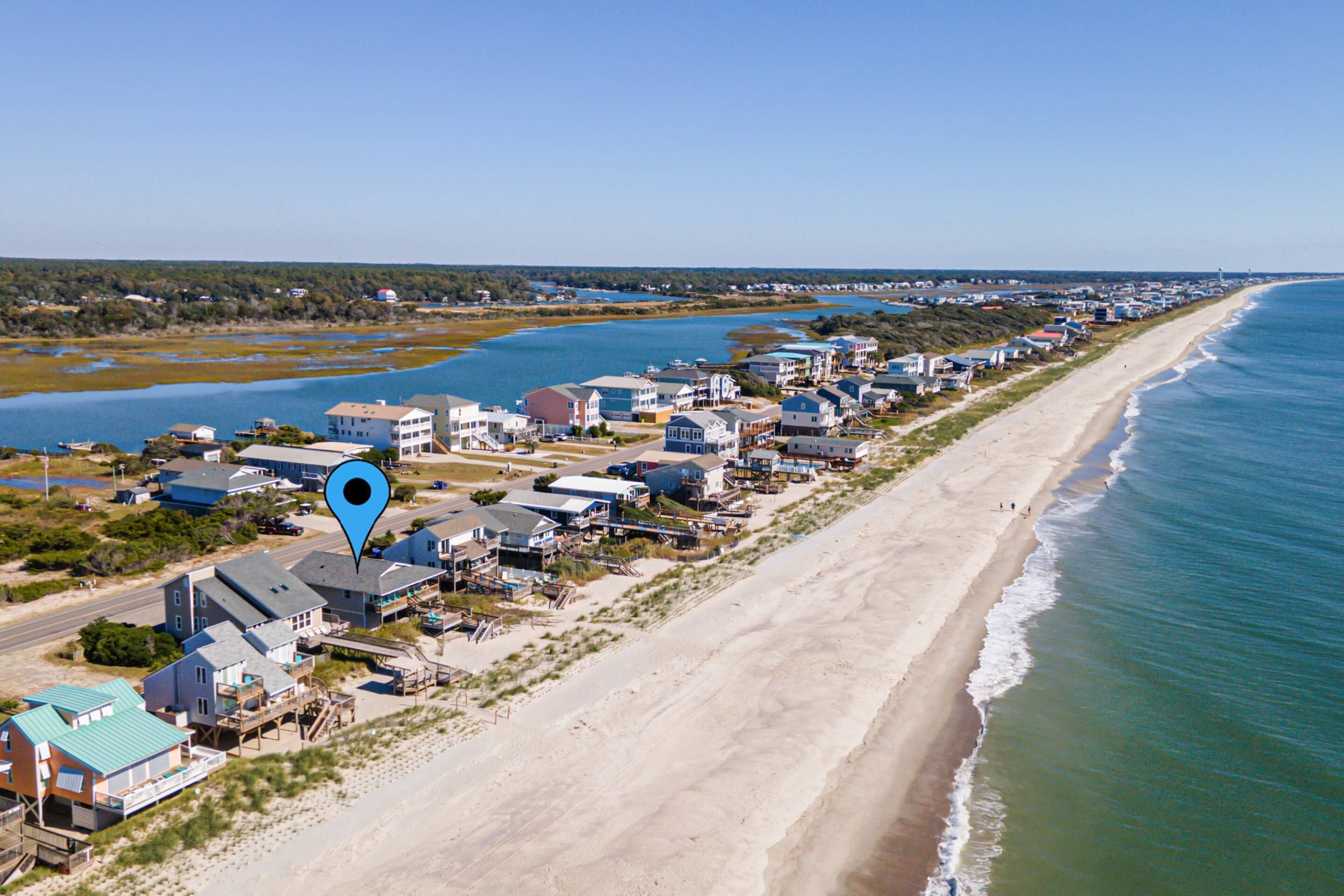 A coastal residential area with houses along the beach, a clear sky, and a body of water in the background.