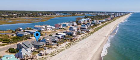 A coastal residential area with houses along the beach, a clear sky, and a body of water in the background.