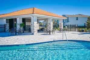 Ein überdachter Außenbereich mit Pool, Steinpfeilern und Gartenmöbeln.