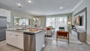 Et moderne køkken med central ø, indbyggede apparater og spiseområde med sofa og stole.