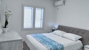 Een slaapkamer met een bed, nachtkastjes, een plant in pot en een plafondlamp.