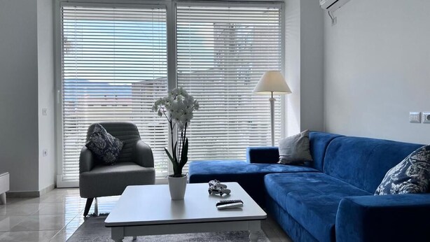 Een woonkamer met een blauwe bank, een grijze fauteuil, een witte salontafel en een lamp.