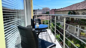 Een balkon met een tafel en stoelen, een glazen deur en uitzicht op gebouwen.