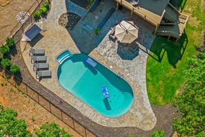 Vue aérienne d’une cour arrière avec une piscine, des chaises longues, un espace salon couvert et une terrasse.